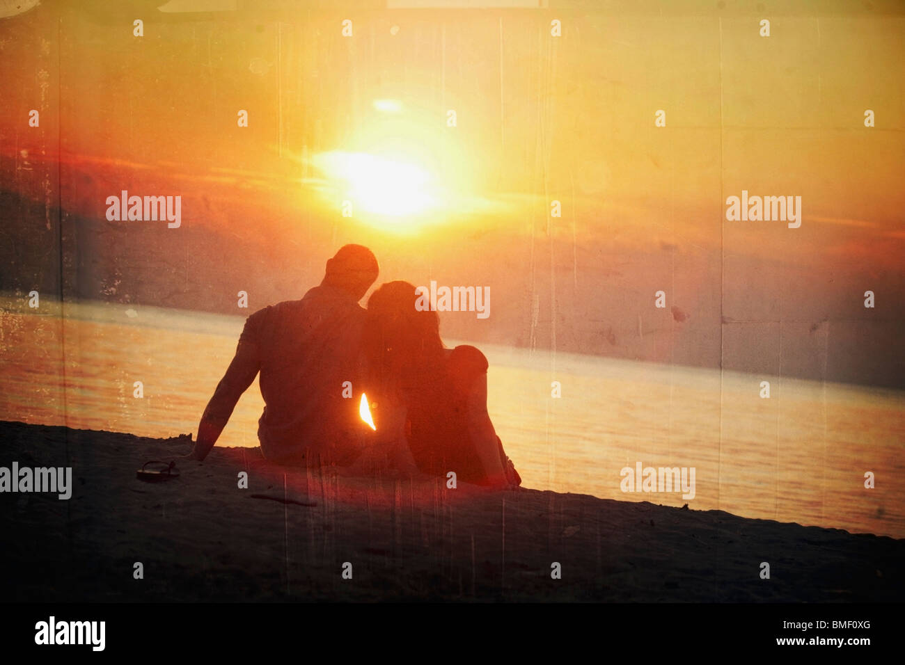 A Man And Woman Sitting On The Beach In A Sunset Stock Photo
