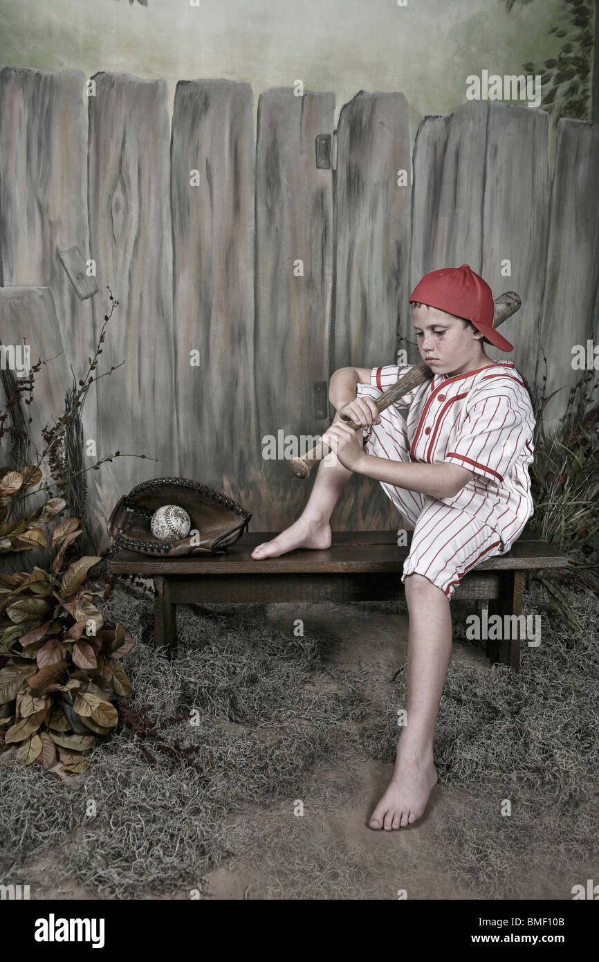 A Boy Holding A Baseball Bat And Wearing A Uniform Sitting On A Bench