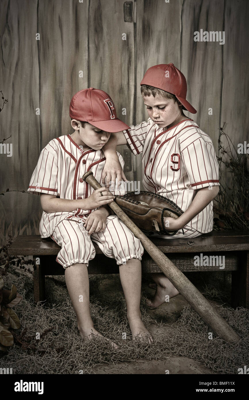 Two Boys In Baseball Uniforms Sitting On A Bench Stock Photo