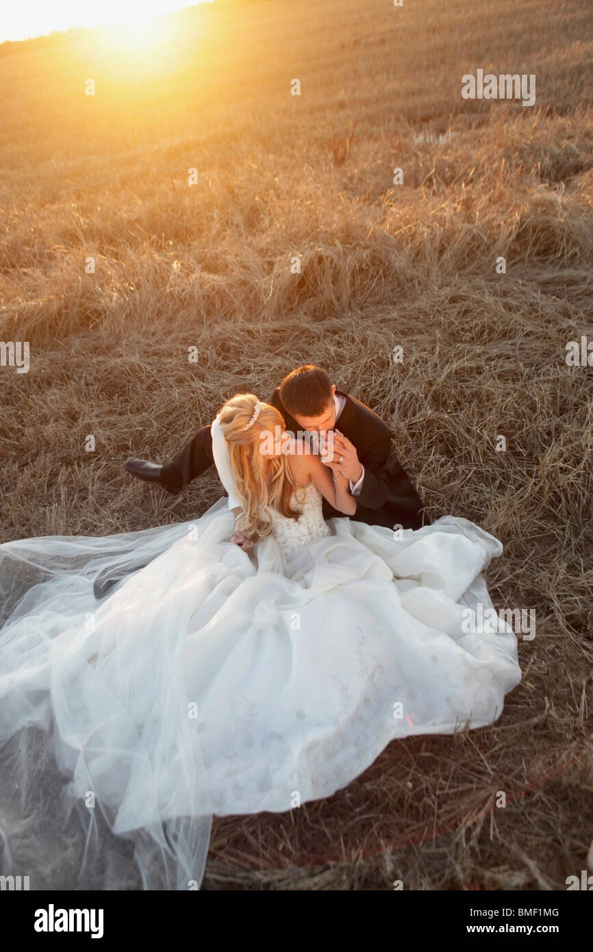 A Bride And Groom Sitting In A Field Stock Photo