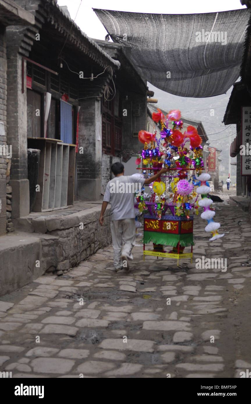 Man walking in stone paved alley with paper flower basket, Qikou Town, Lin County, Luliang City, Shanxi Province, China Stock Photo
