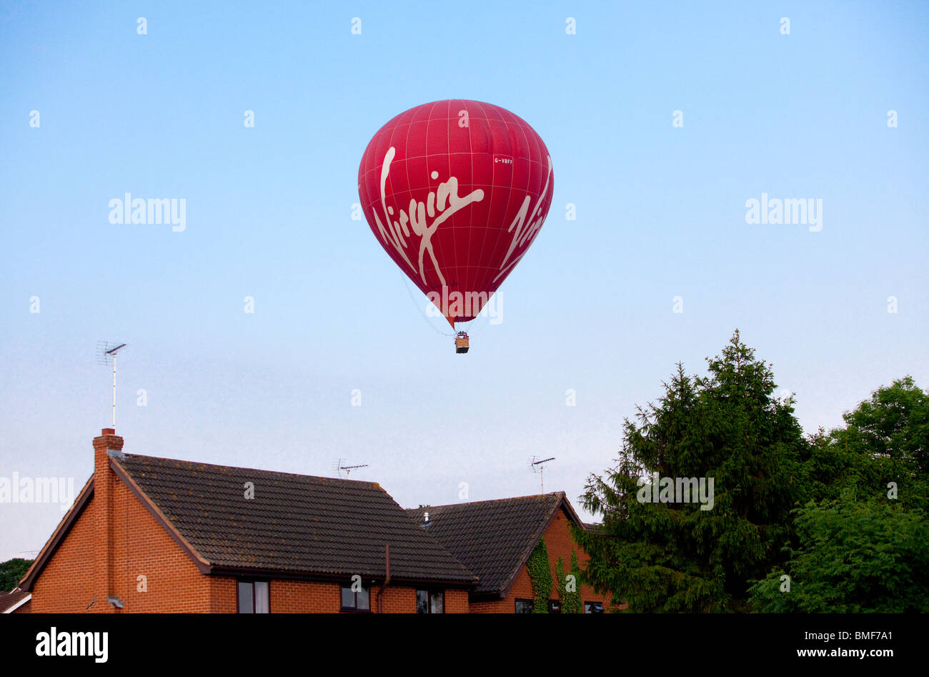 A red hot air balloon flying low over residential houses in