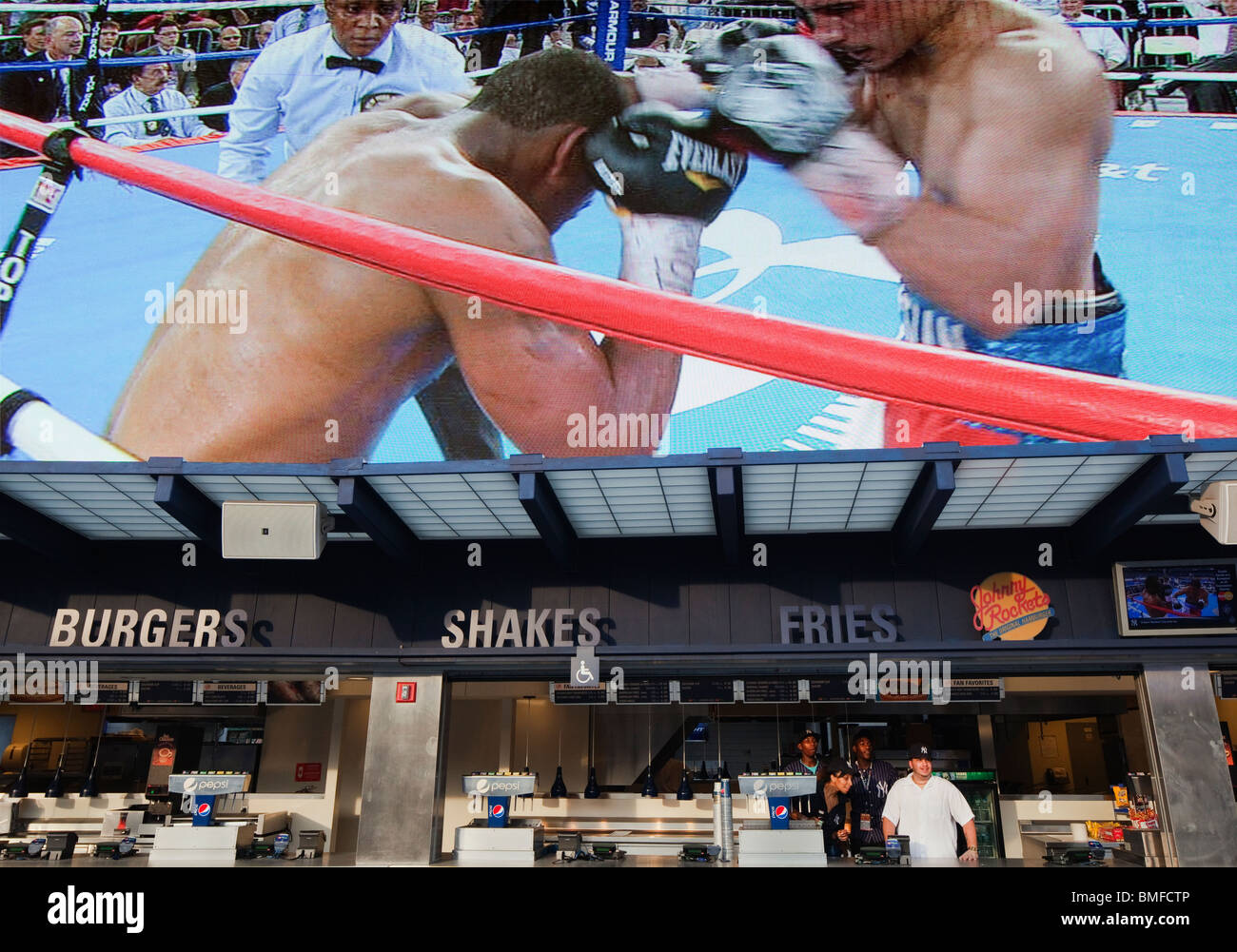 Yankee Stadium food stand workers look onto to a boxing match as the mega screen above them replays the action. Stock Photo