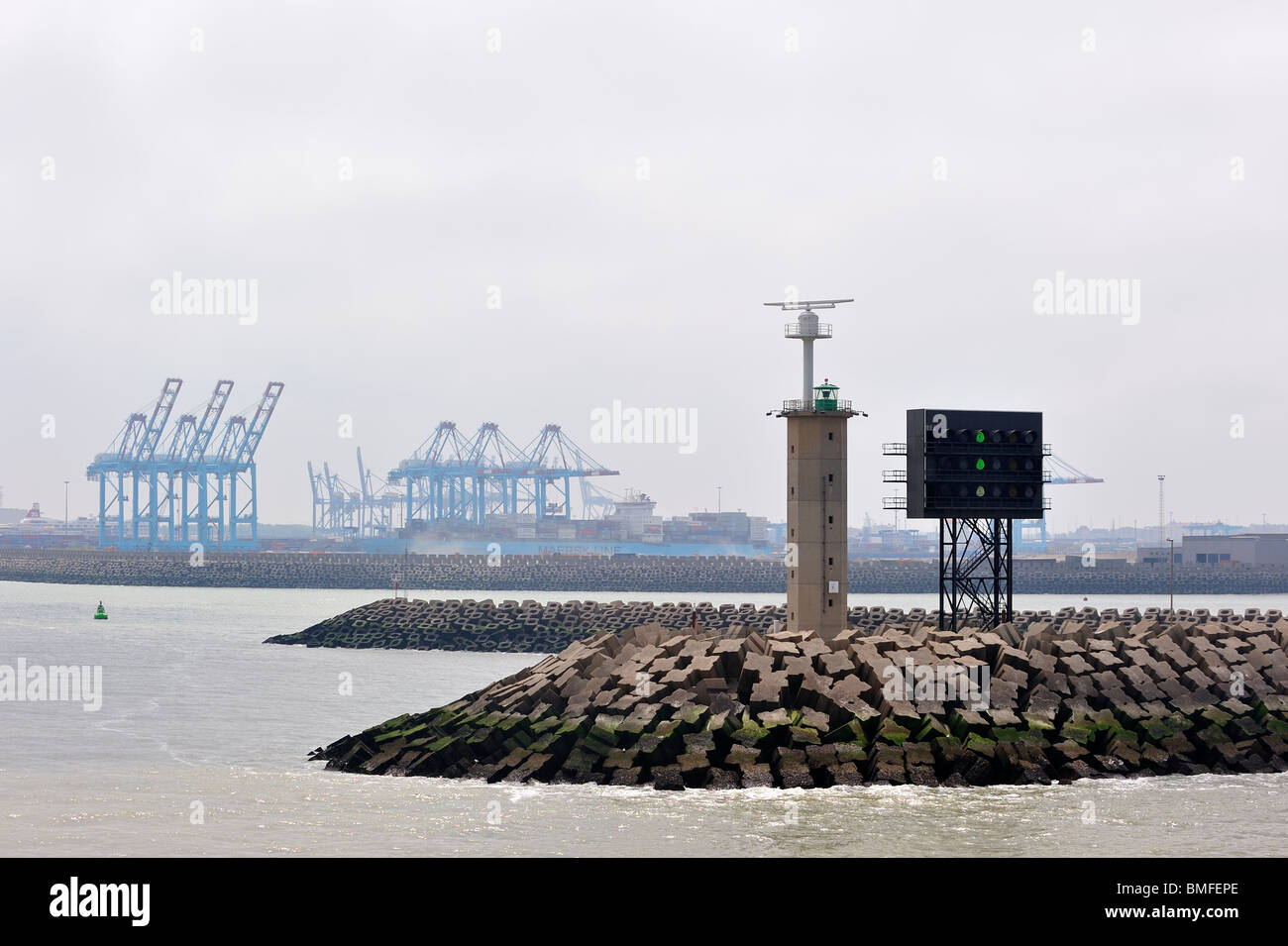 Mole with signal light at the harbour / dock entrance and container terminal cranes of the Port of Zeebrugge, Belgium Stock Photo
