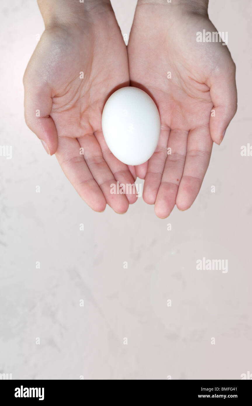 A conceptual image of a young woman's hands holding an egg against a beige background. Concept fertility, concept reproduction. Stock Photo