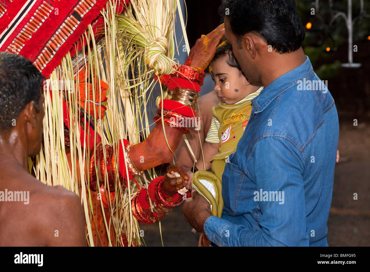 India, Kerala, Cannanore (Kannur), Theyyam, serpent deity Naga Kanni giving young child it’s first blessing Stock Photo