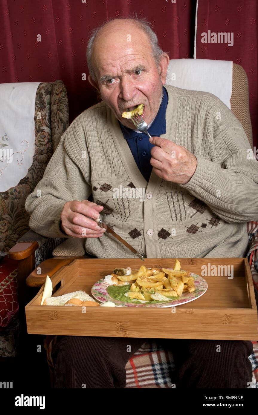 Elderly man eating fish and chips while watching TV. Stock Photo