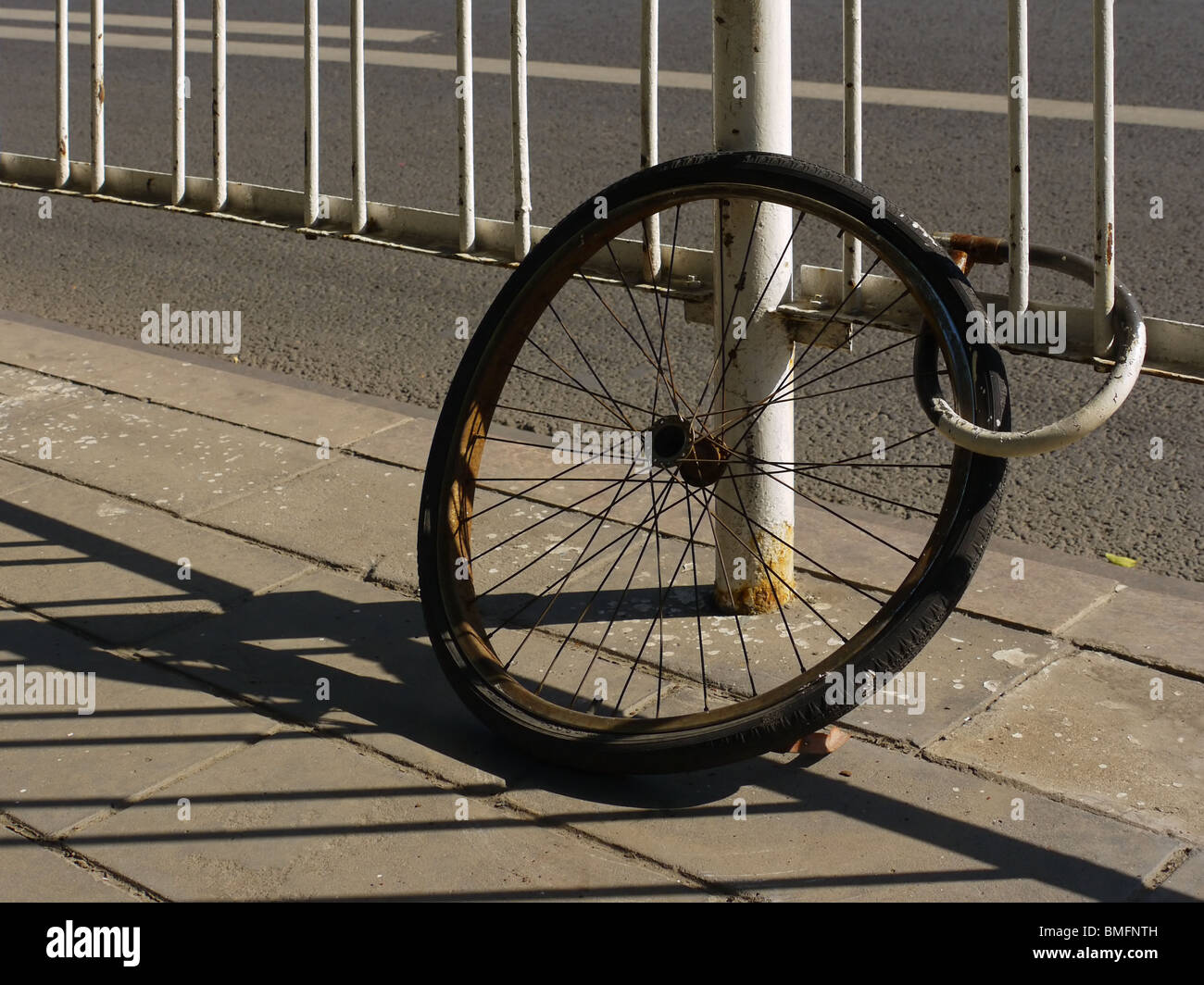 Lonely rusty bicycle wheel remains padlocked for ages to the highway fence in Beijing, China Stock Photo
