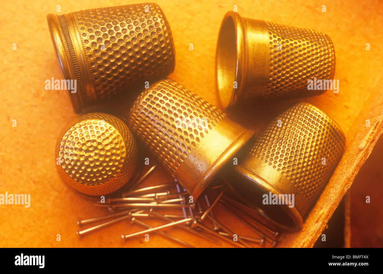 Close up of five brass thimbles with pins in corner of cardboard tray