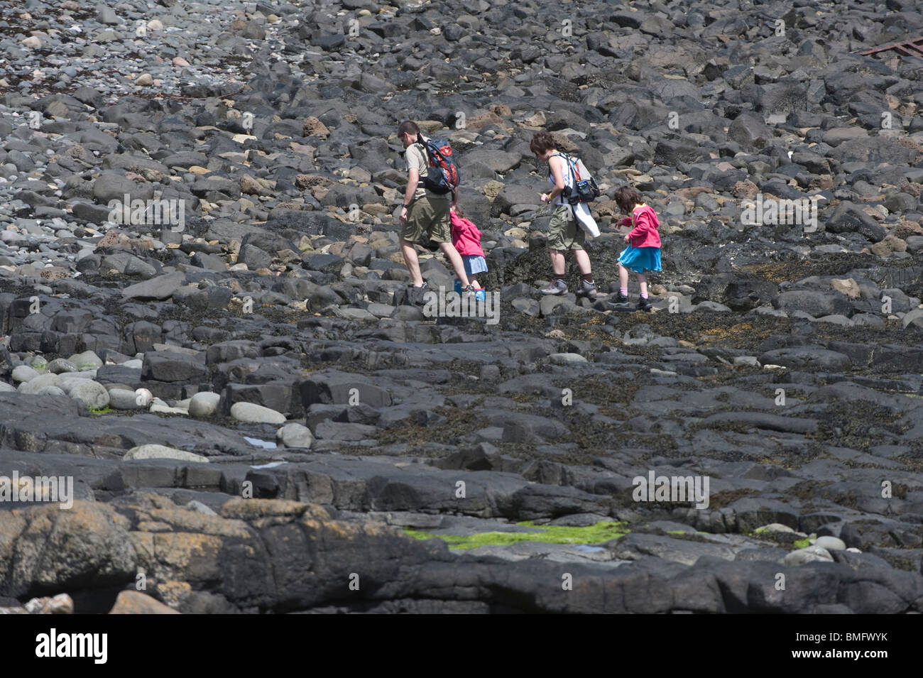 Family with two children walking on boulders near Dunstanburgh Castle Craster Northumberland coast England UK Europe Stock Photo