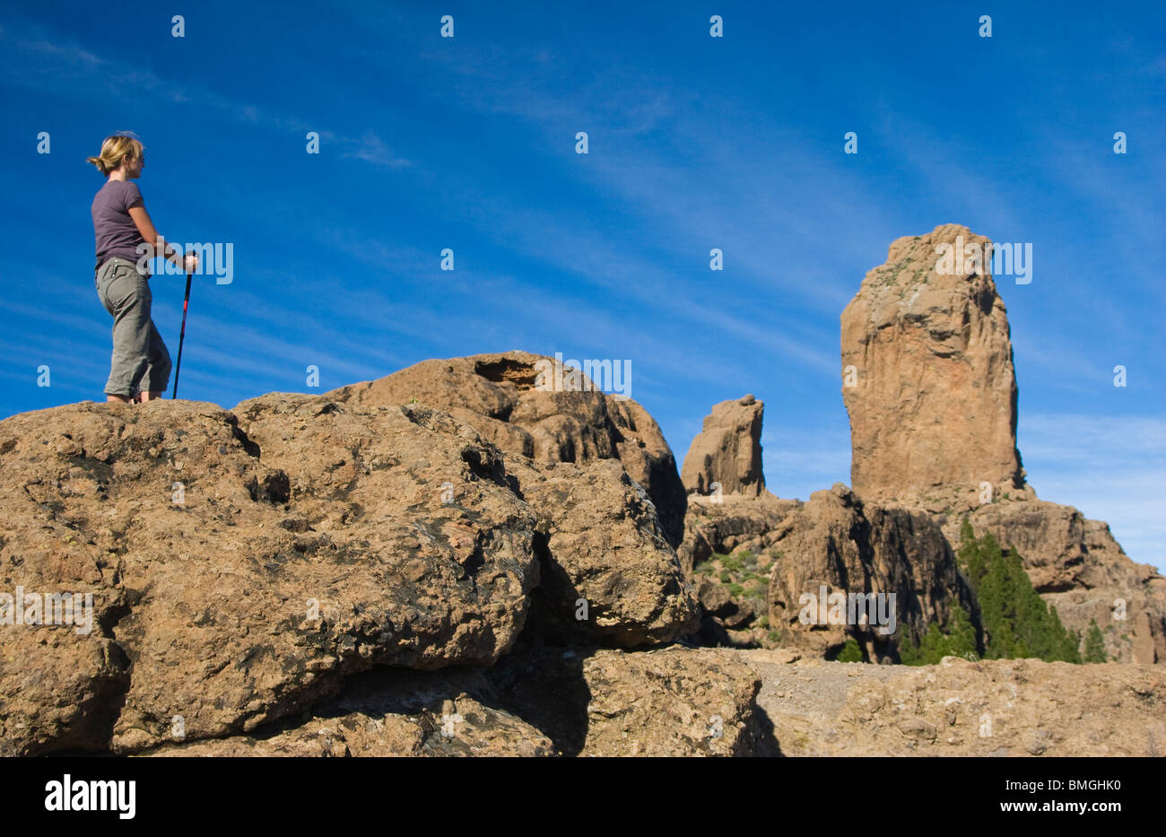 Woman with a Nordic walking pole looking at Roque Nublo or Cloud Rock in the mountains or Cumbres of Gran Canaria Stock Photo