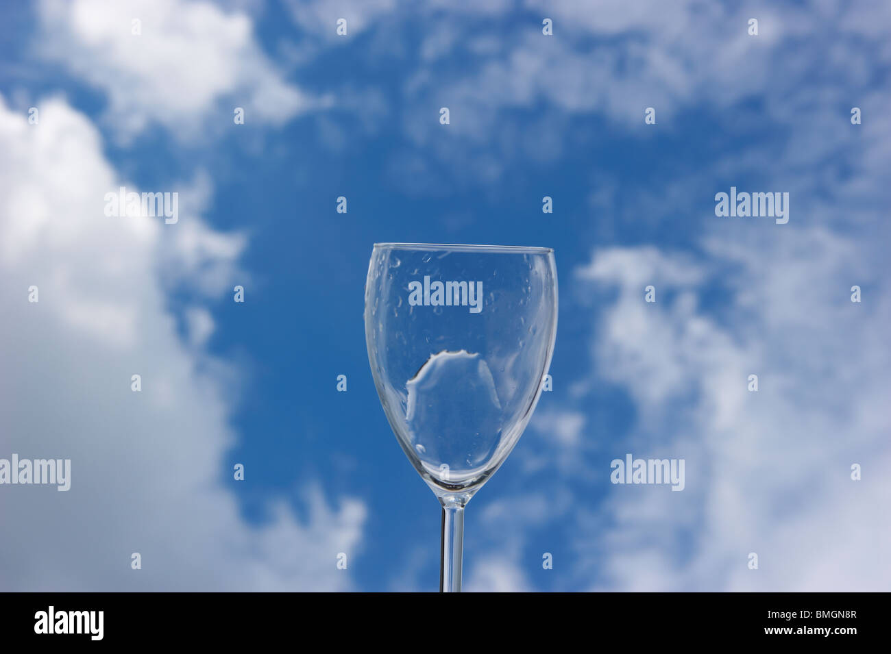 water streams out of an glass in front of a blue cloudy sky Stock Photo