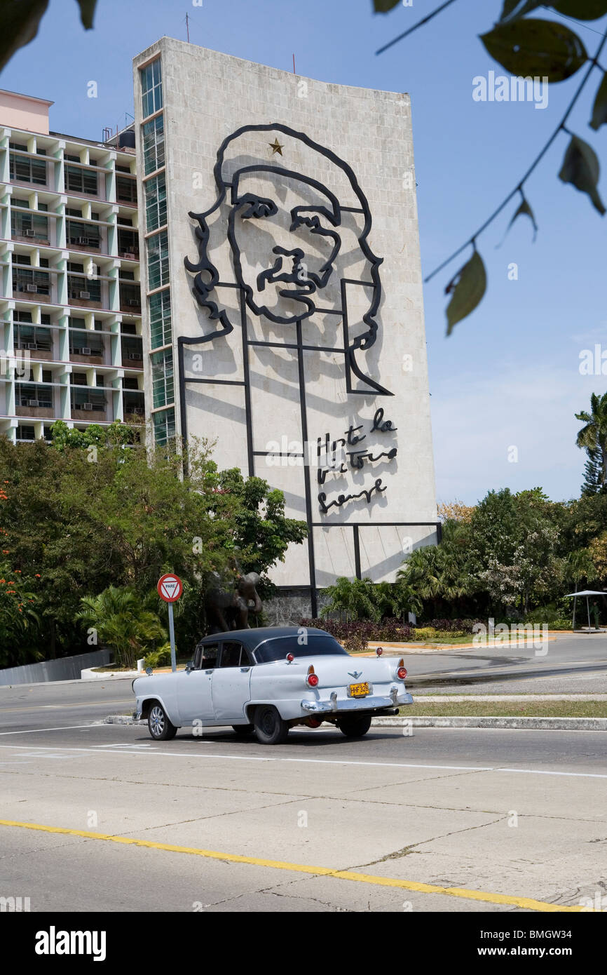 A classic car in Cuba passes a building with an image of Che Guvera. Stock Photo