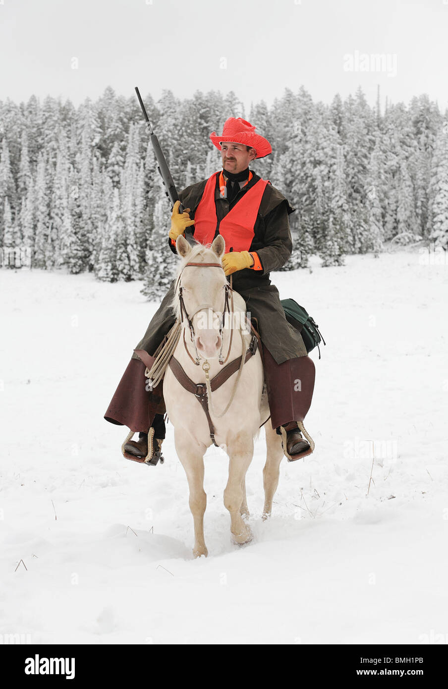 cowboy hunter riding white horse in snow hunting with rifle Stock Photo