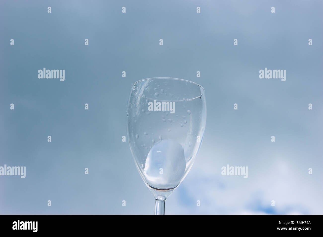 water streams out of an glass in front of a blue cloudy sky Stock Photo