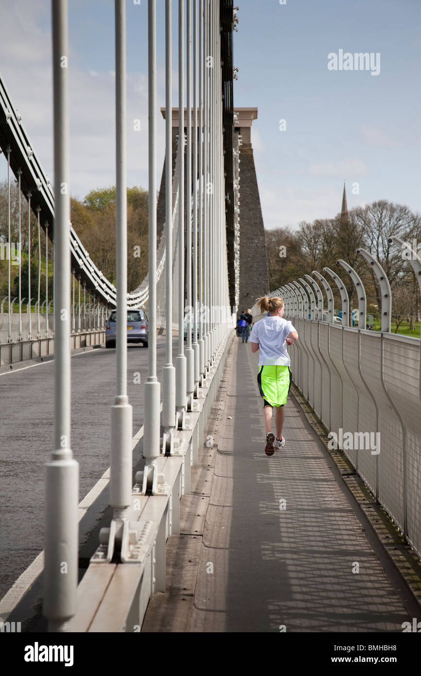 A jogger runs along the pathway on the Clifton Suspension Bridge with the 'anti suicide' barrier to her right. Bristol, England. Stock Photo