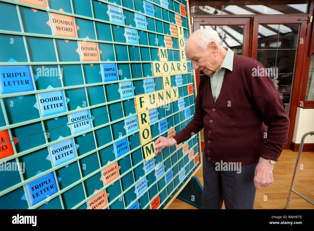 An old man playing with a giant scrabble board one of the many activities on offer in care homes to keep people's minds active Stock Photo