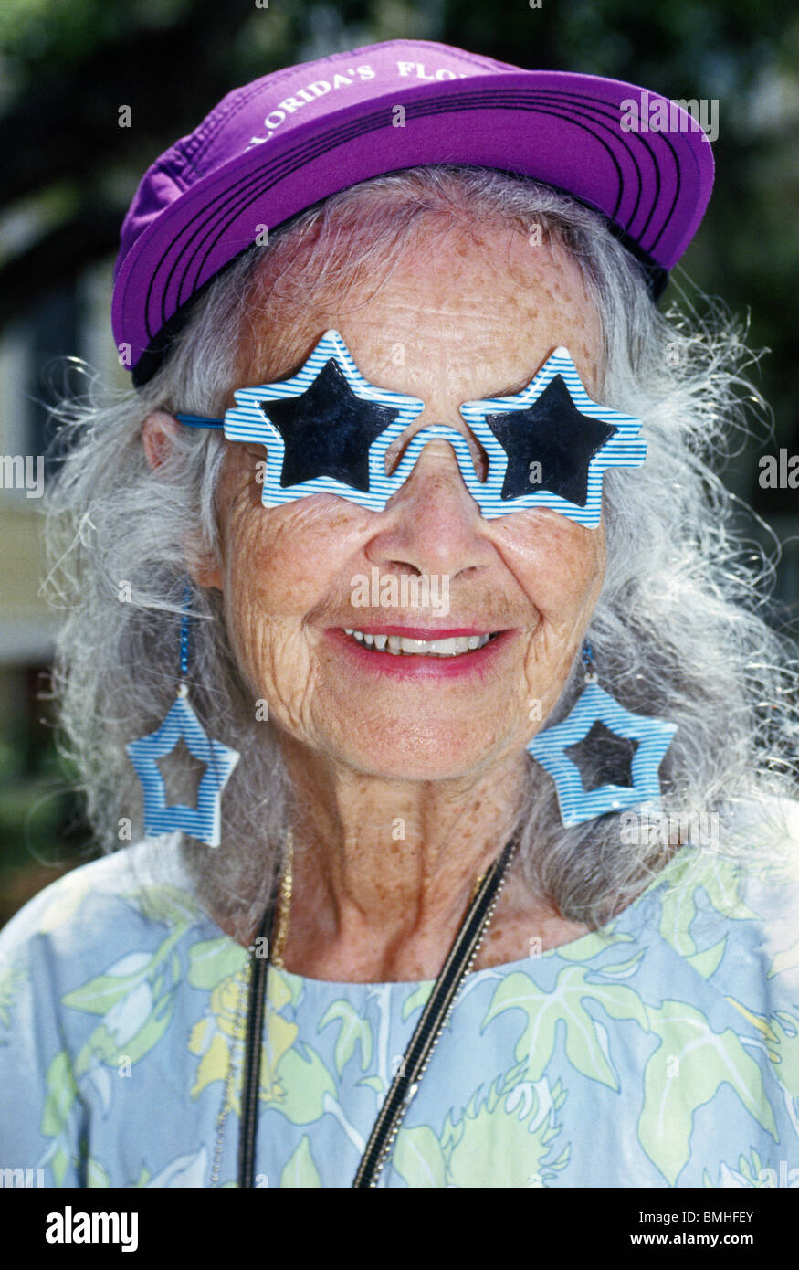 A spunky senior American woman shows off her star-shaped sunglasses and matching earrings while on vacation in Florida, the Sunshine State. Stock Photo