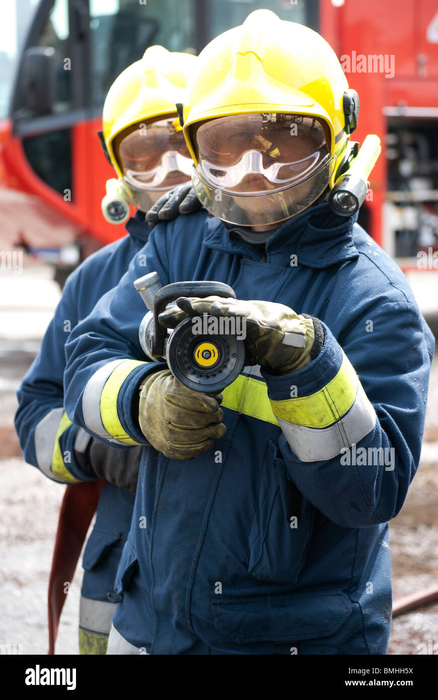Two firefighters holding water hose fire truck in background Stock