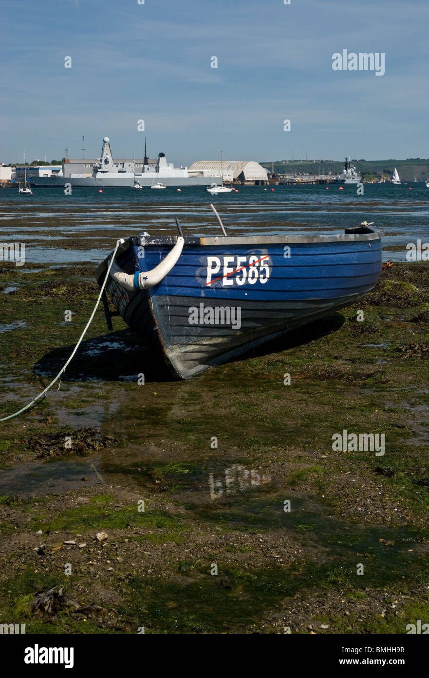 A small wooden boat moored at shore with the Destoyer Daring in the background Stock Photo