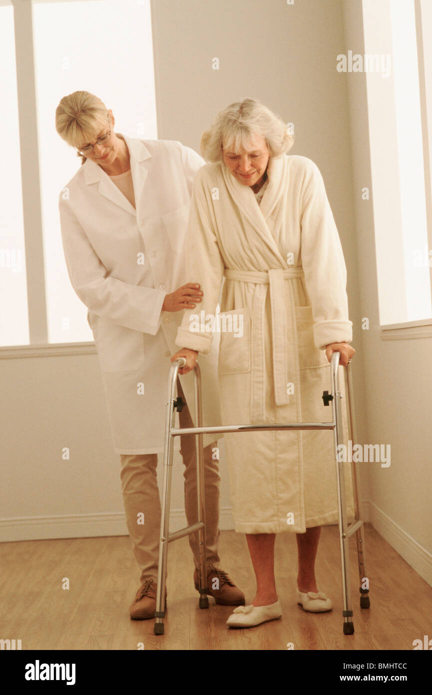 Healthcare worker helping a woman walk with a walker Stock Photo - Alamy