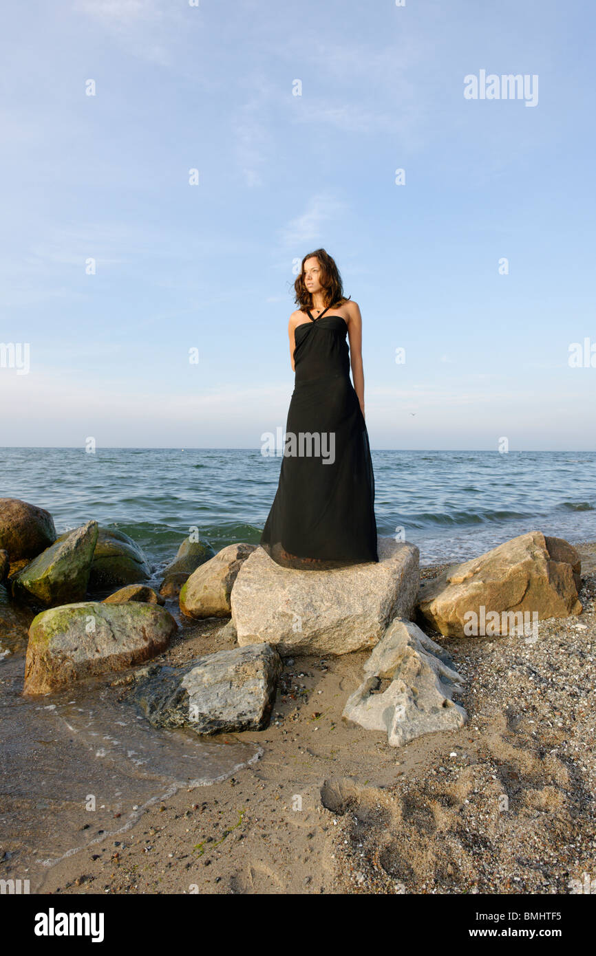 Young woman, 20+, standing like a statue on a beach, wearing a black dress, lifestyle, Niendorf on the Baltic Sea, Germany Stock Photo