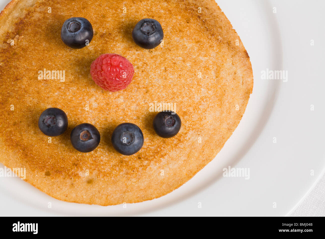 Pancake with smiley face made from blueberries and raspberry Stock Photo