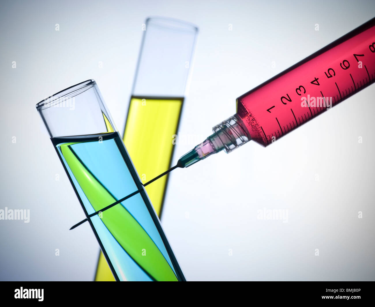 A syringe and two test tubes filled with color liquids. Stock Photo