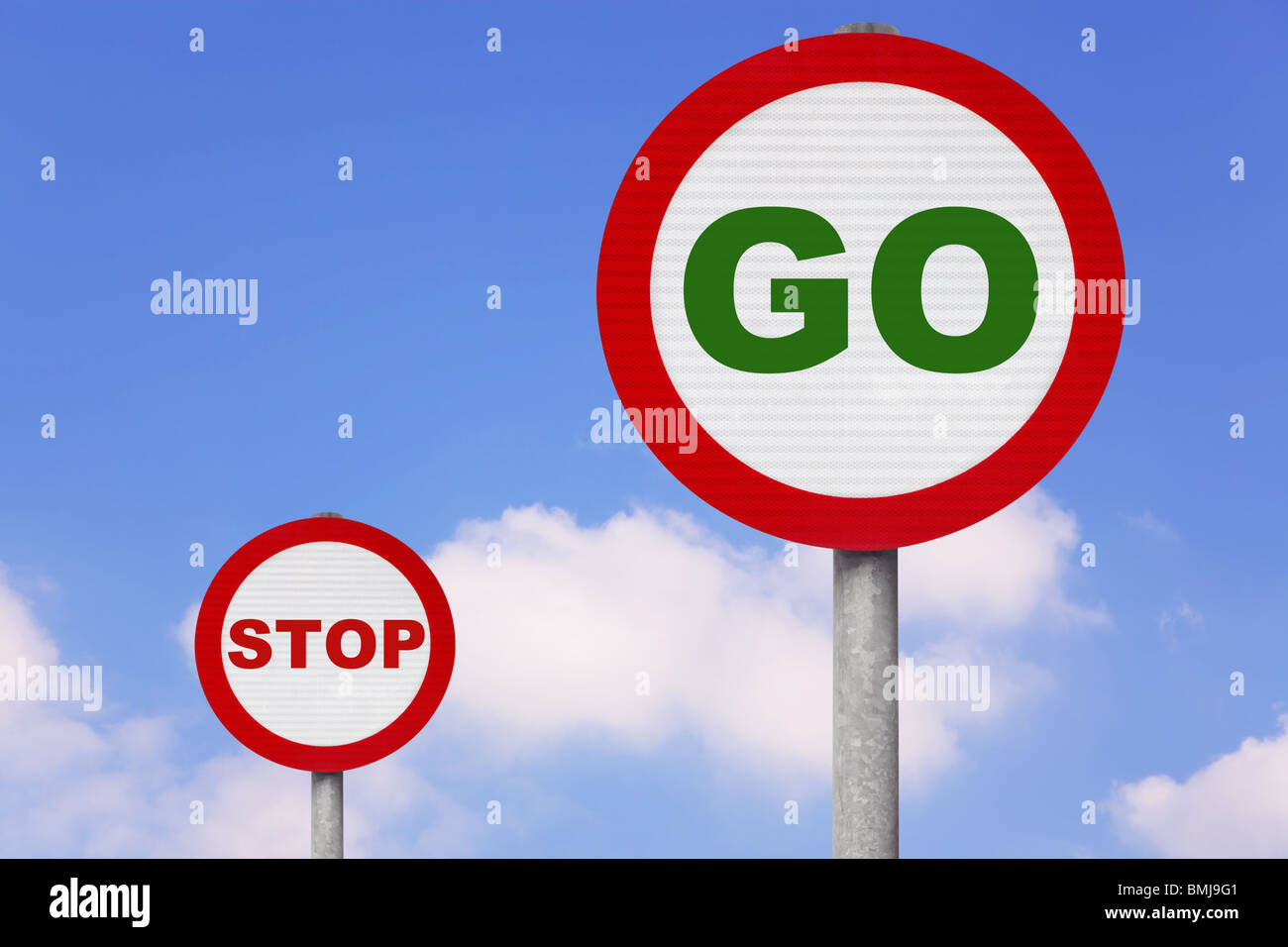 Round roadsigns with GO and STOP on them against a blue cloudy sky. Stock Photo