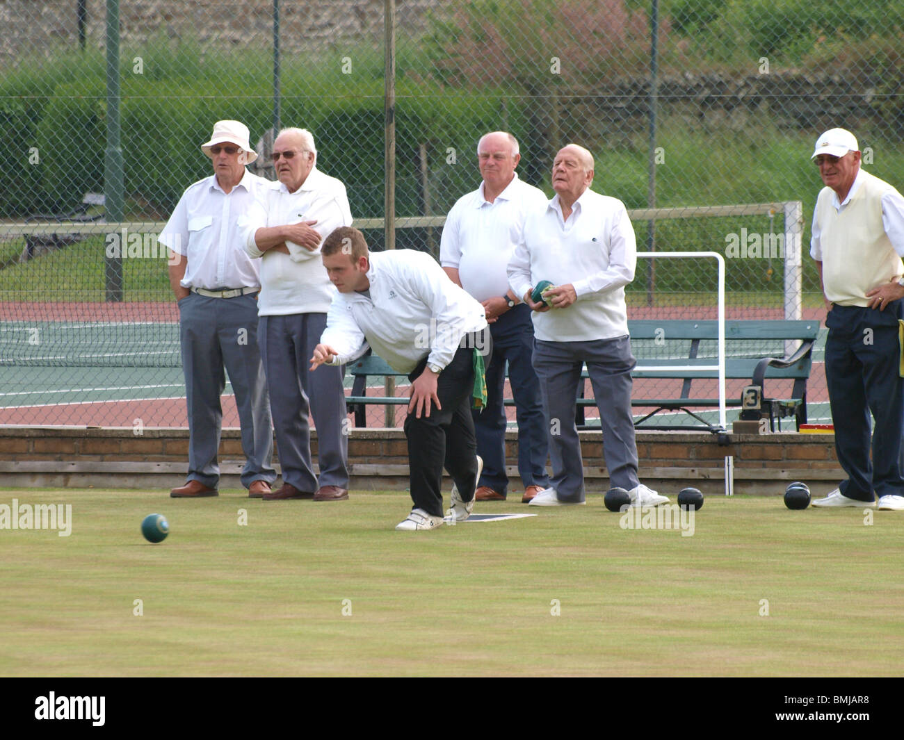 Young man playing bowls with a group of old men, Bude, Cornwall Stock Photo