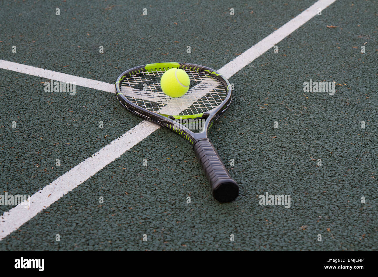 Tennis racket (racquet) and ball on white T line of a tennis court on