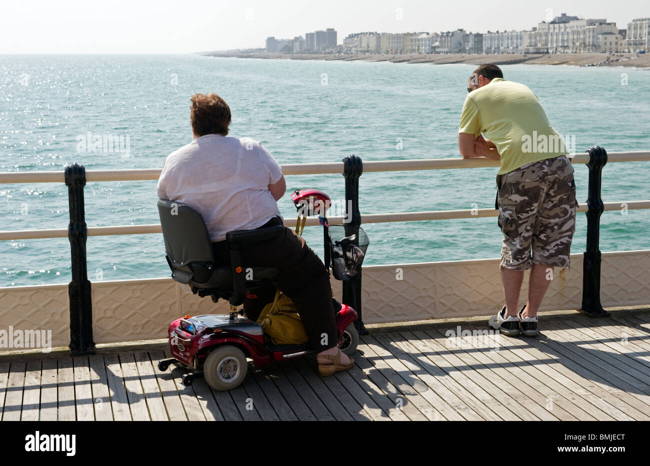 A man leaning on iron railings and a disabled woman on Worthing pier on ...