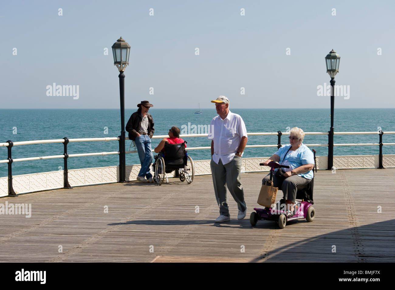 An elderly couple passing by a man talking to a disabled person in a wheelchair on Worthing pier. Stock Photo