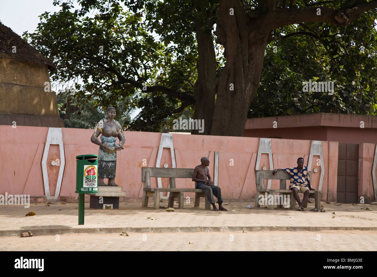 Africa, West Africa, Benin, Ouidah. Men sitting on benches beside statue in Ouidah, Benin. Stock Photo