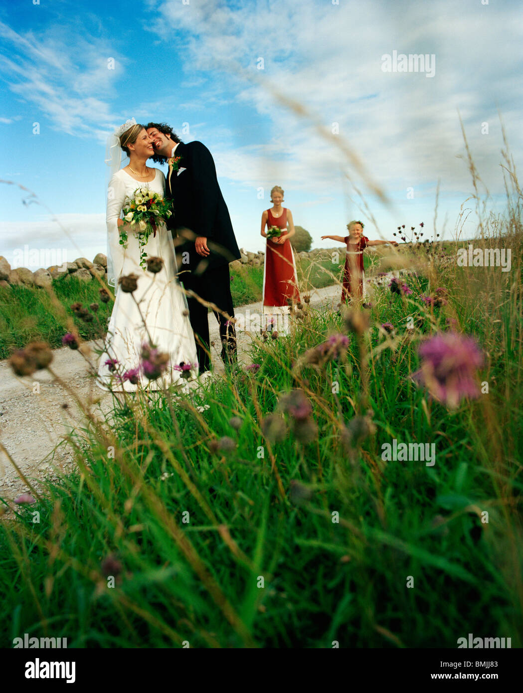 Scandinavia, Sweden, Oland, Bride and groom kissing with bridesmaid and flower girl in background Stock Photo