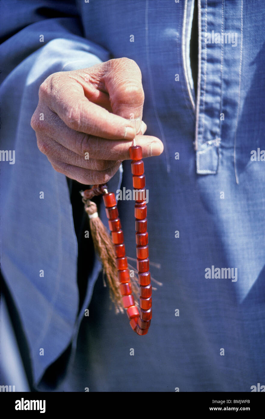 In Aswan, Egypt, a close-up of a man's hand holding a string of red prayer beads and wearing a blue galabeya. Stock Photo