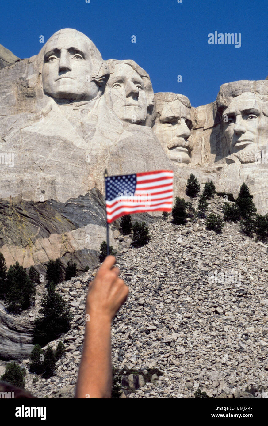 A visitor to Mount Rushmore National Memorial waves an American flag to salute four U.S. Presidents sculpted on a mountainside in South Dakota, USA. Stock Photo