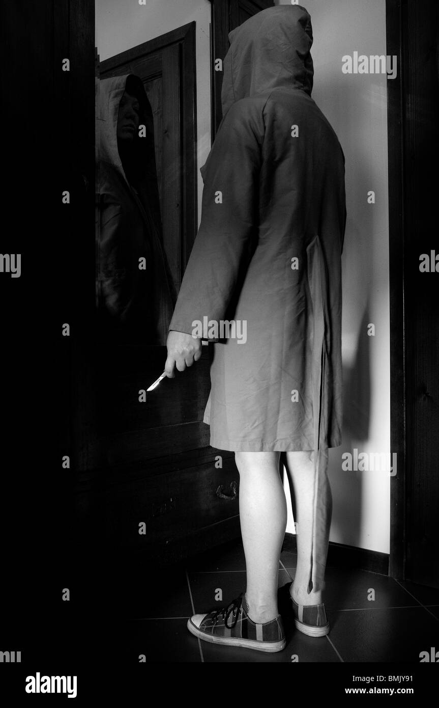 Hooded woman with knife in front of the mirror Stock Photo