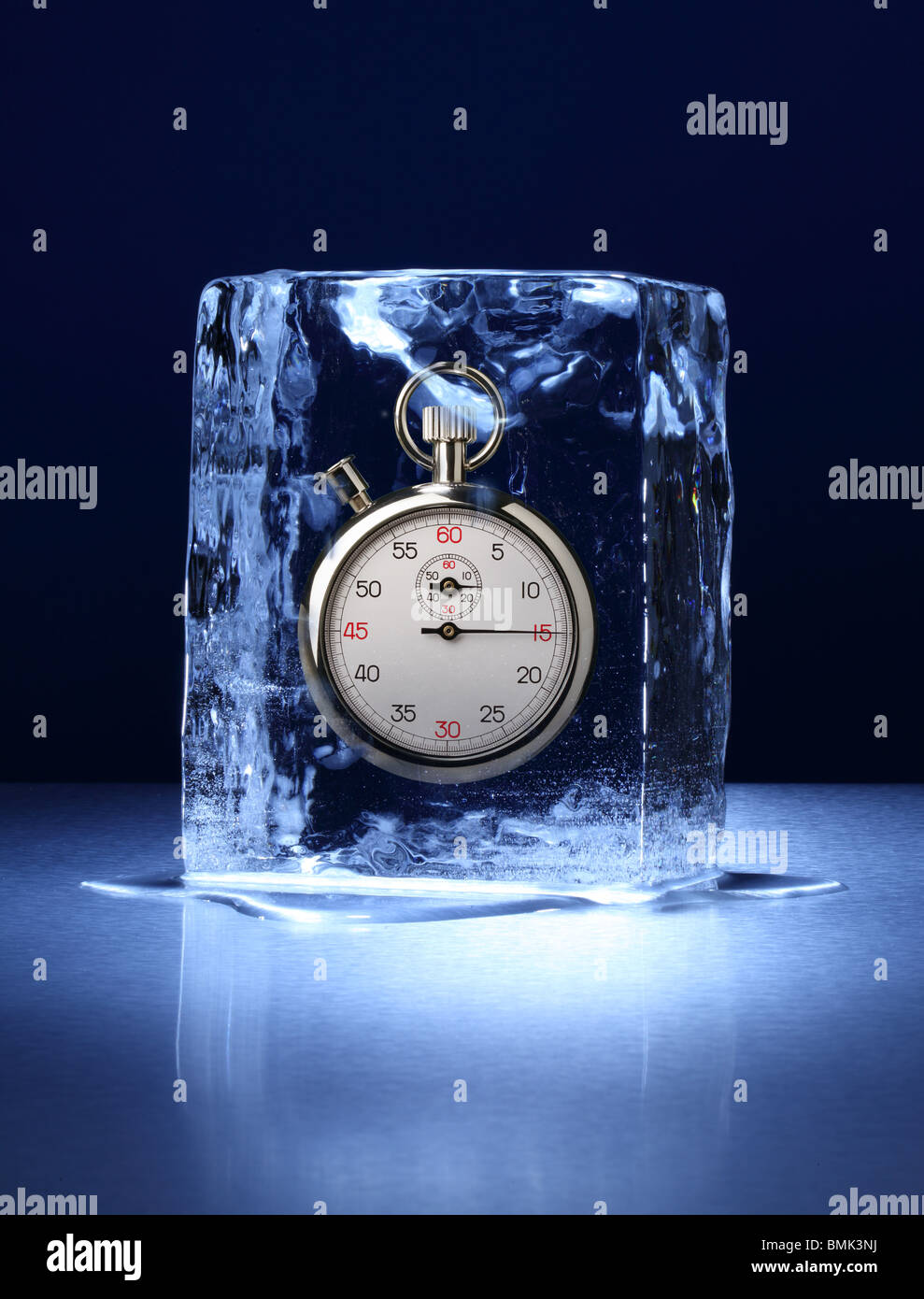 A frozen block of ice with a stopwatch frozen inside on a metal surface Stock Photo