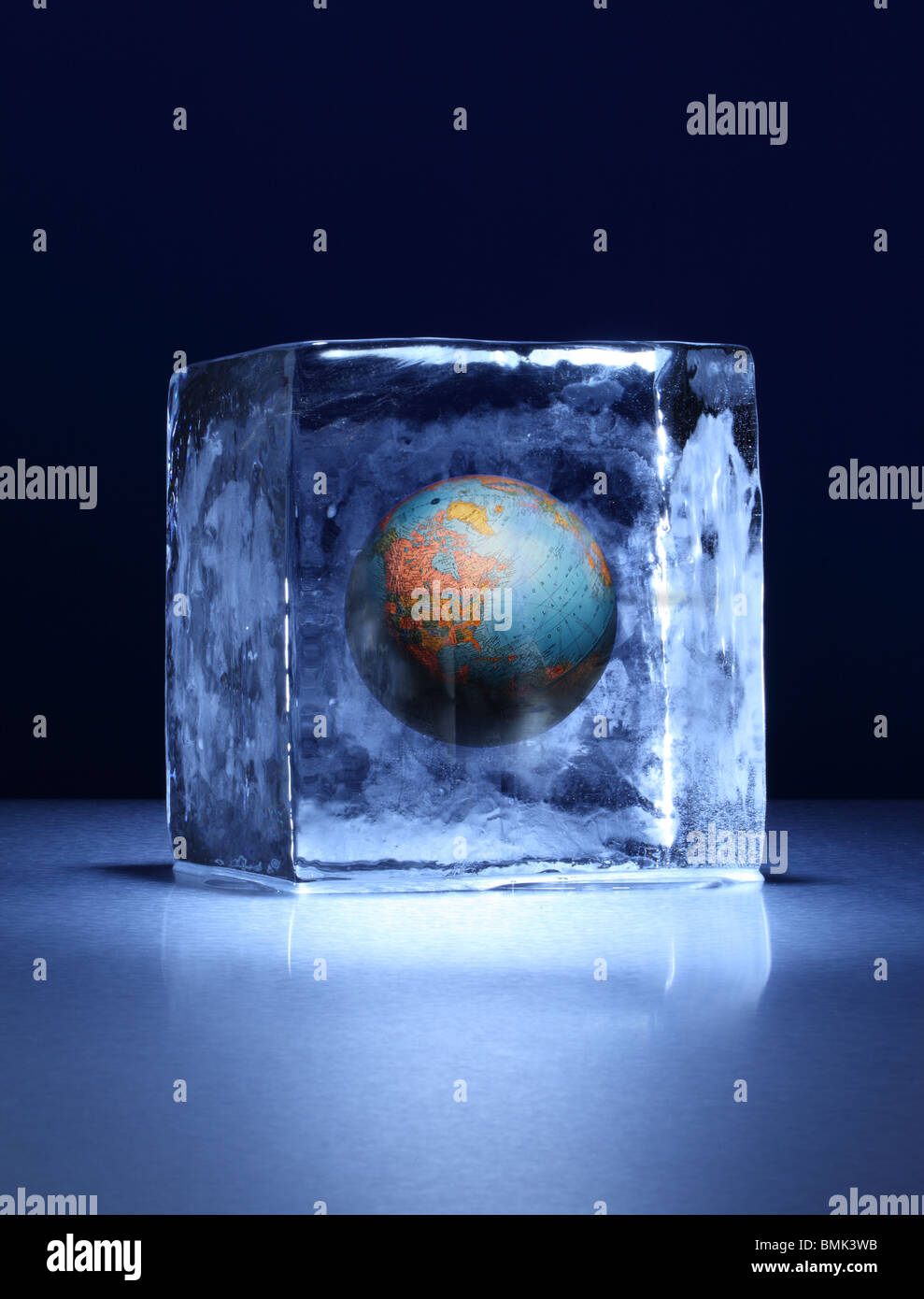 A frozen block of ice with a world globe frozen inside on a metal surface Stock Photo