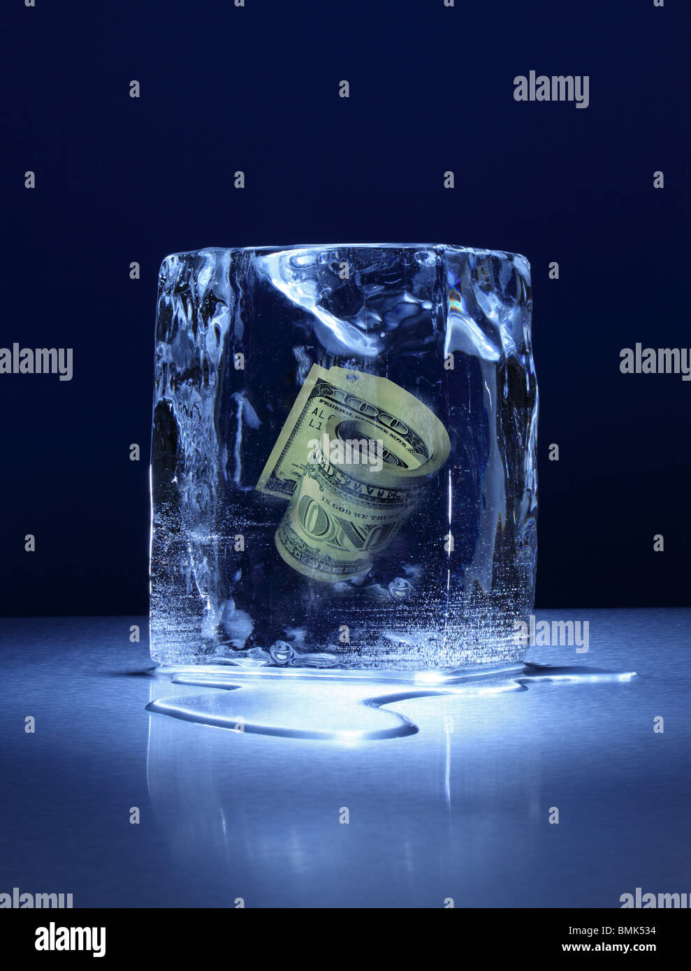 A frozen block of ice with a roll of US cuurency frozen inside on a metal surface Stock Photo