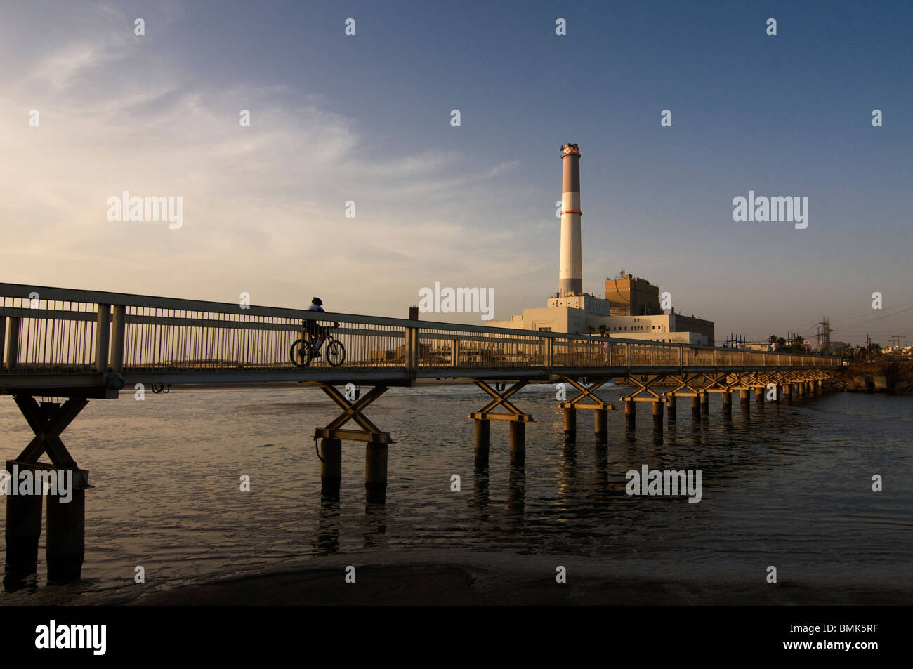 Bicycler crossing a bridge over the Yarkon or Yarqon river near Reading power station supplying electrical power to the Tel Aviv district in Israel Stock Photo