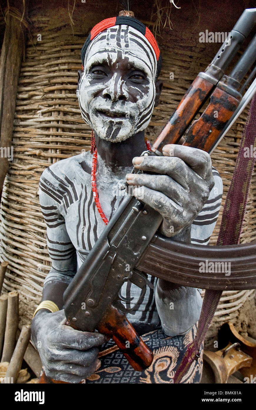 Ethiopia Lower Omo River Basin Chelete a Duss tribal communitiy man with body and face paint holding AK 47 in front of granary Stock Photo