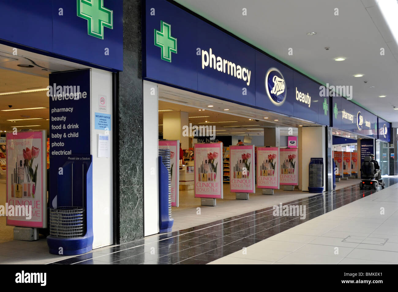 Green Pharmacy Cross signs above open plan entrances to Boots chemist retail business with beauty store in shopping centre mall Chelmsford England UK Stock Photo