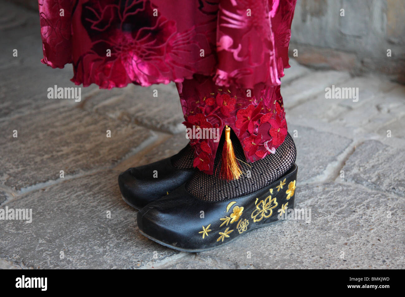 The feet of a local woman in a Bokhara market in Uzbekistan wearing traditional national dress with embroidered clogs. Stock Photo