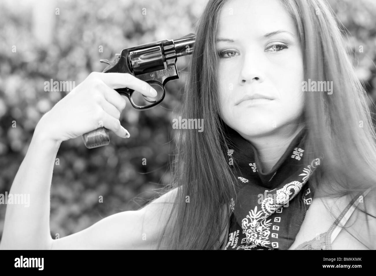 Attractive Brunette Woman in Blue Bandanna Points Pistol at self in a suicidal pose Stock Photo