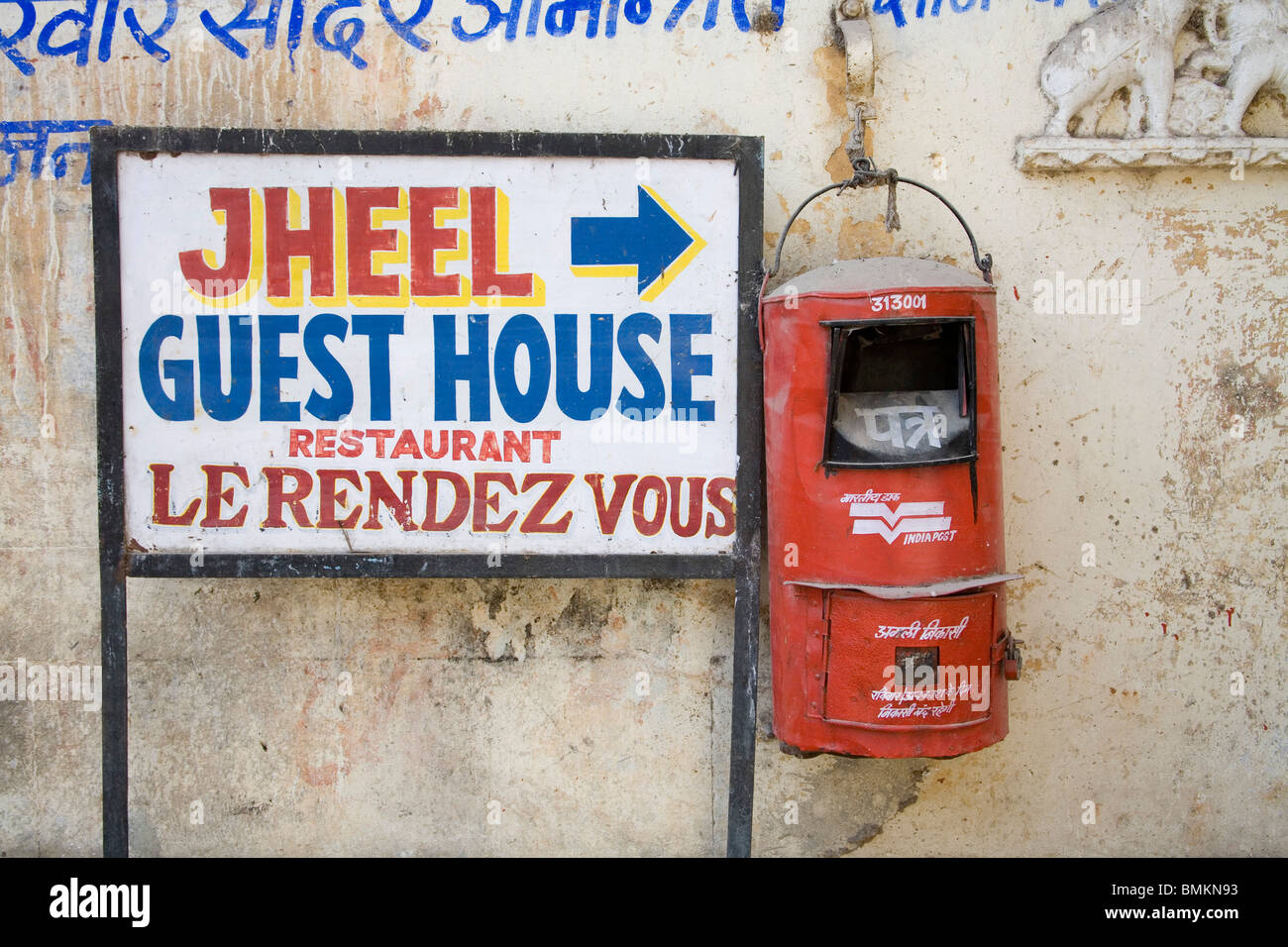 Red color letterbox of Indian postal services with near jheel guest House board ; Udaipur ; Rajasthan ; India Stock Photo