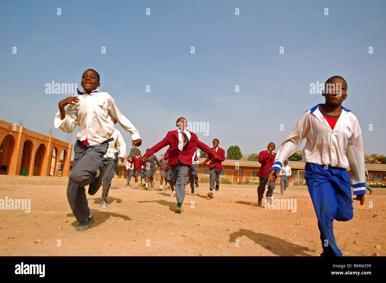 Nigeria, Jos, Schoolboys and schoolgirls in their purple and blue school uniform, running alltogether on a sandy field. Stock Photo