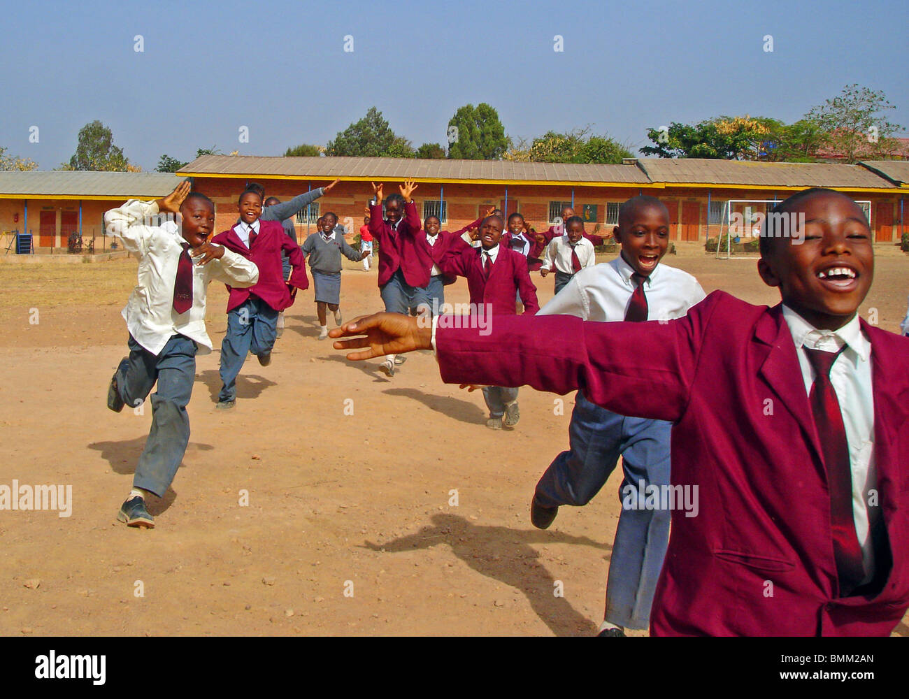 Nigeria, Jos, Schoolboys and schoolgirls in their purple and blue school uniform, running alltogether on a sandy field. Stock Photo