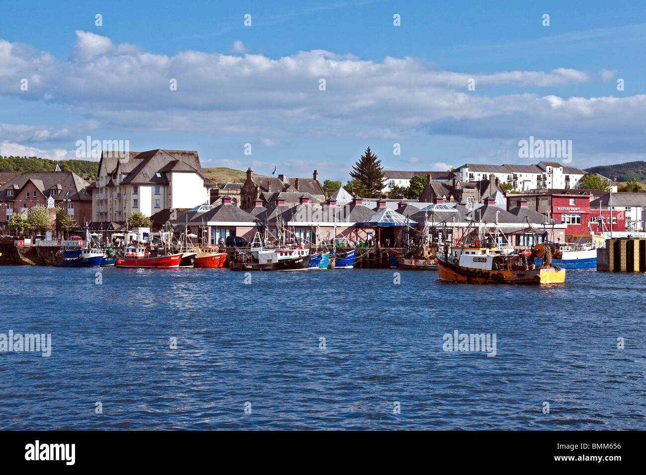 A fishing boat is arriving in Oban Harbour Lorn Scotland with other boats already moored along the pier. Stock Photo